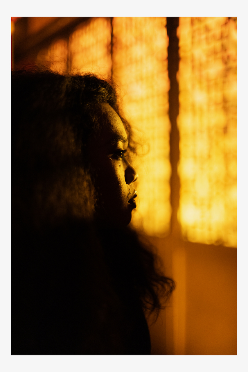 A person in profile by a glowing amber window