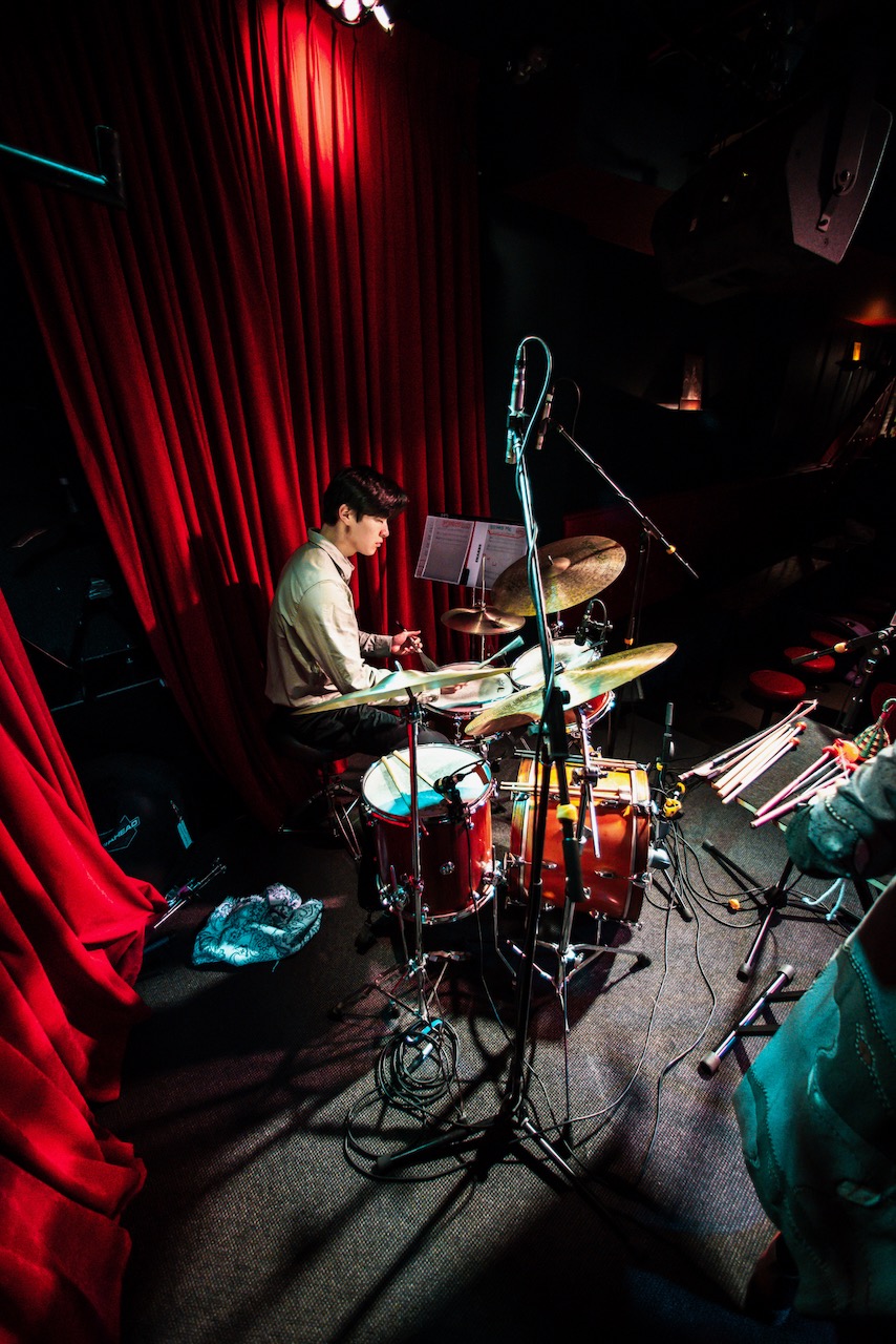 A drummer performing beside red curtains