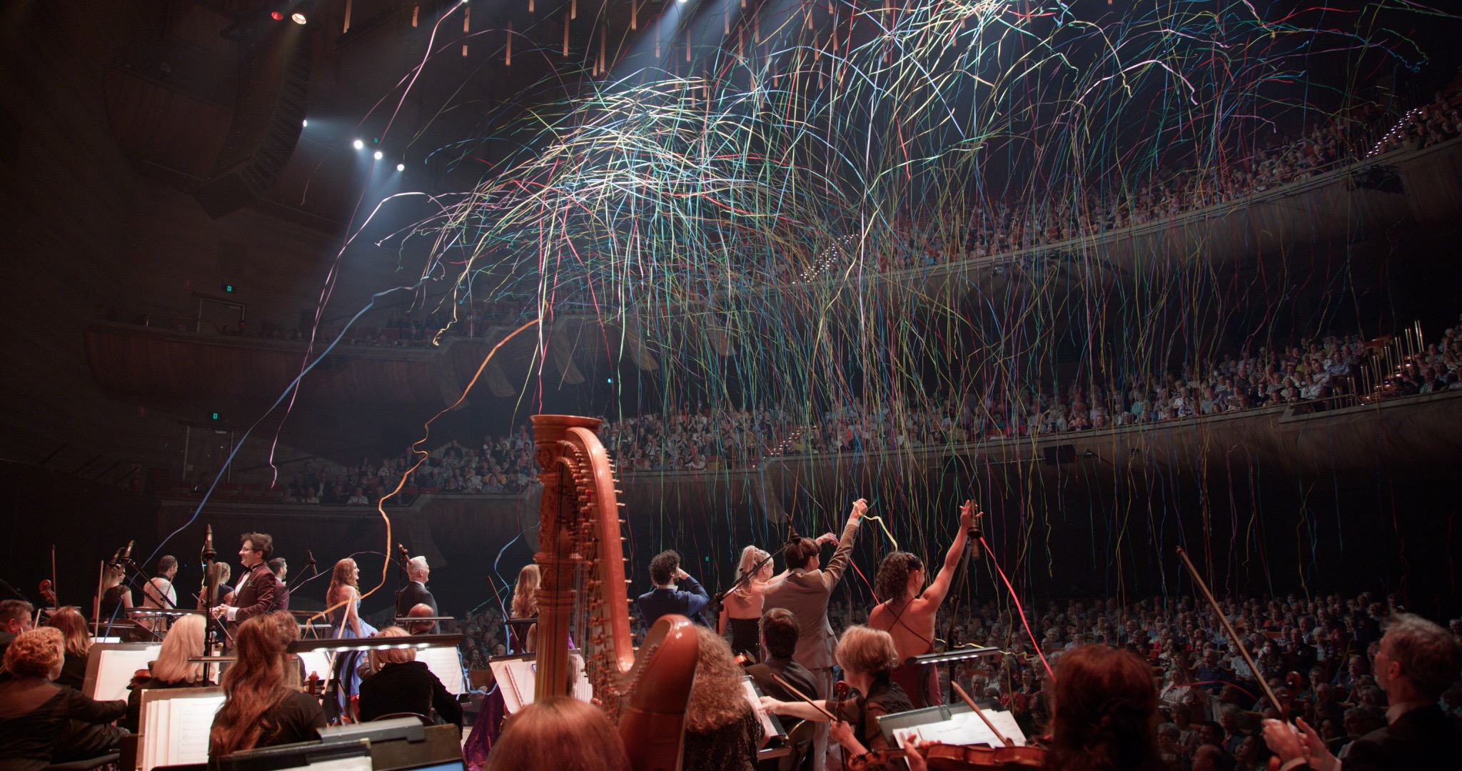 An orchestra in performance beneath a concert hall light show